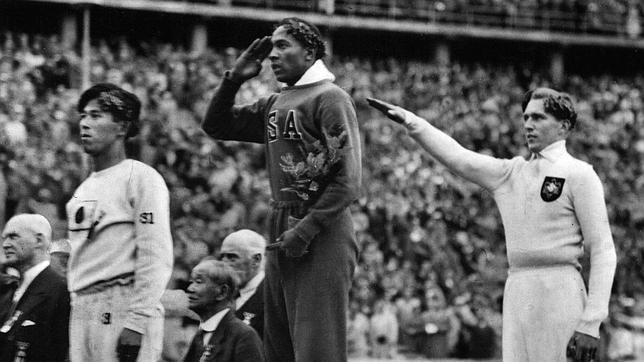 Juegos de Berlín 1936. Jesse Owens escucha el himno estadounidense desde lo alto del podio. Detrás, Lutz Long hace el saludo nazi