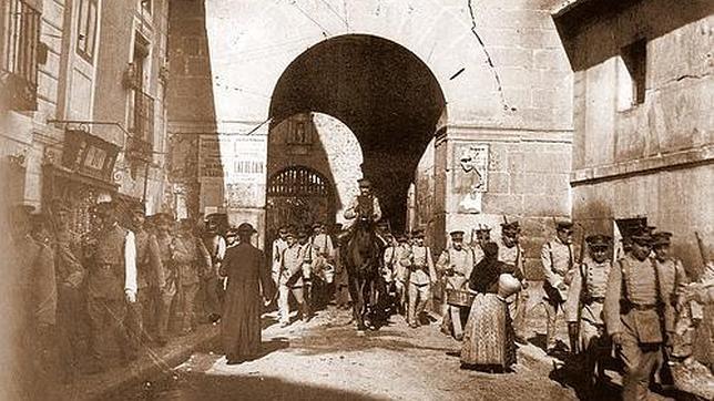 La imagen está tomada antes de 1934; un cura pasea junto a varios militares por la puerta de Bisagra