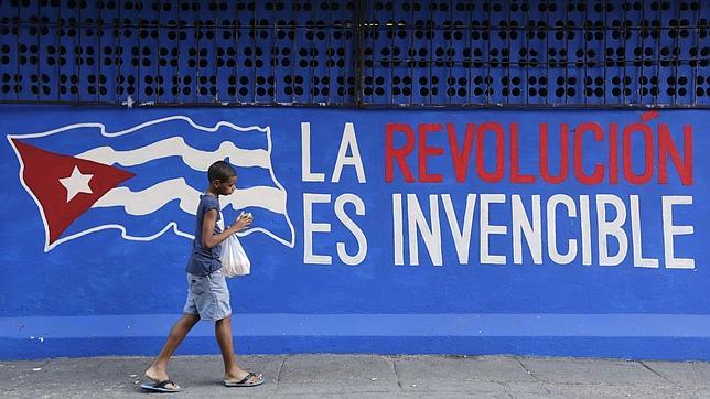 Un muchacho pasea junto a un grafiti por las calles de La Habana