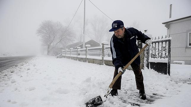 Un hombre retira la nieve con una pala en la entrada de su casa en Maceda