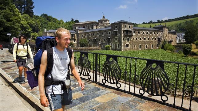 Dos peregrinos con mochilas pasan frente al monasterio de Samos