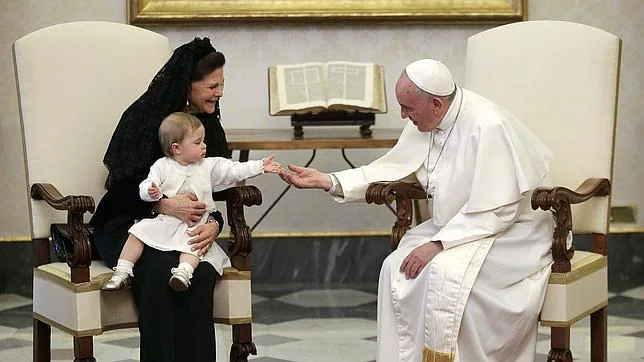 El Papa Francisco juega con Leonore de Suecia, sentada en el regazo de su abuela, la Reina Silvia de Suecia