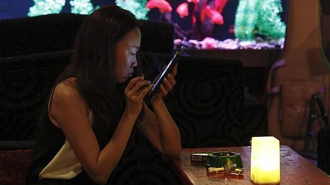 Una mujer sostiene un cigarrillo mientras mira su móvil en un bar de una zona turística de Pekín