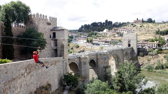 Un usuario se desliza por la tirolina con el puente de San Martín al fondo