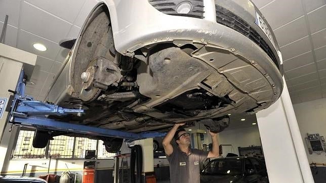 Un mecánico inspecciona los bajos de un coche en su taller