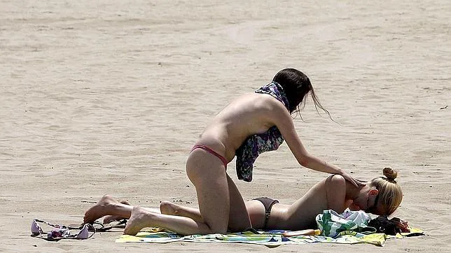 Una joven pone crema solar a otra en la playa