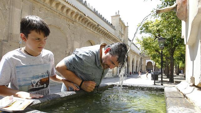 Un hombre y un niño se refrescan en una fuente de Córdoba