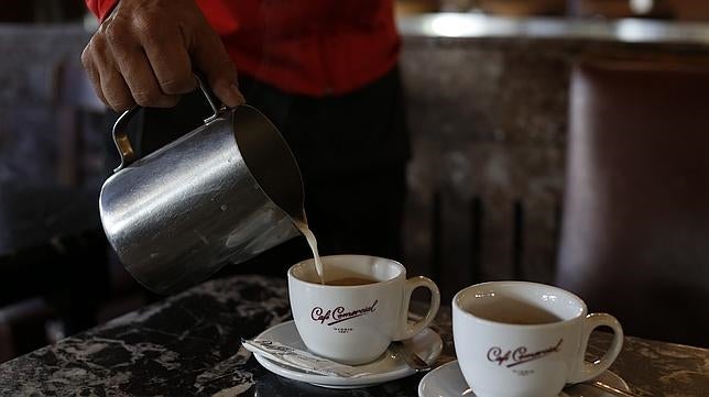 Una empleada vierte una taza de café con leche a un cliente
