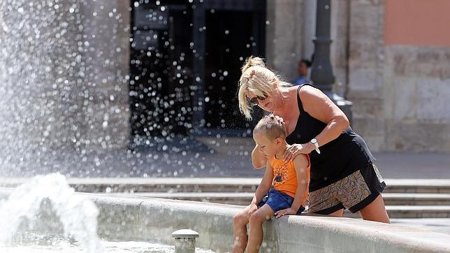 Una madre refresca a su hijo en la fuente de la Plaza de la Virgen de Valencia