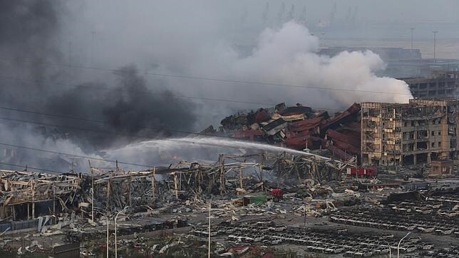 Los bomberos sofocan el fuego entre edificios y vehículos destruidos, tras las explosiones en Tianjin (China)