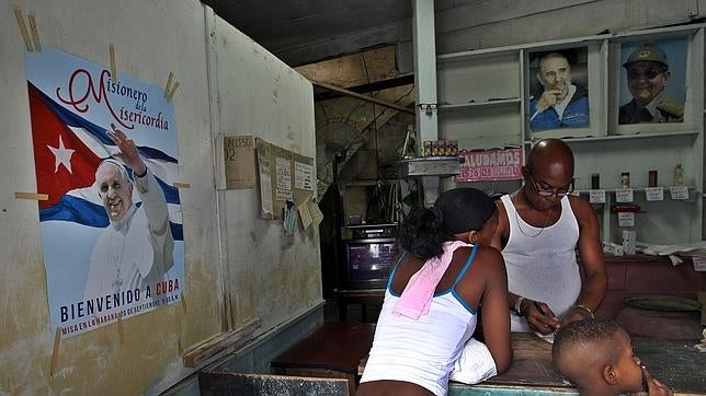 Una mujer compra en un bodega, en la que aparecen un cartel de la visita del Papa y retratos de los líderes cubanos