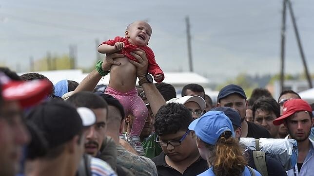 Un inmigrante sostiene a su bebé en alto mientras espera recibir el permiso para subir a un tren en dirección a Serbia en Gevgelija (Macedonia)