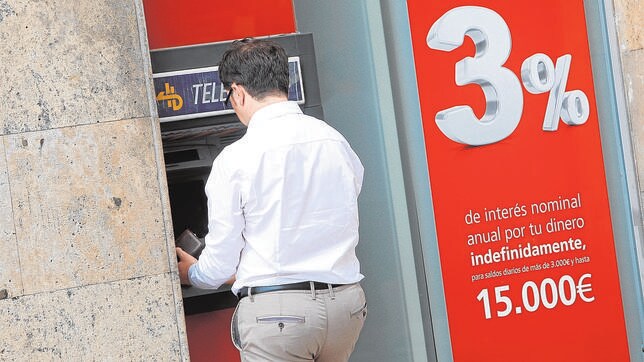 Un hombre saca dinero de un cajero en Valencia junto a una publicidad para captar depósitos