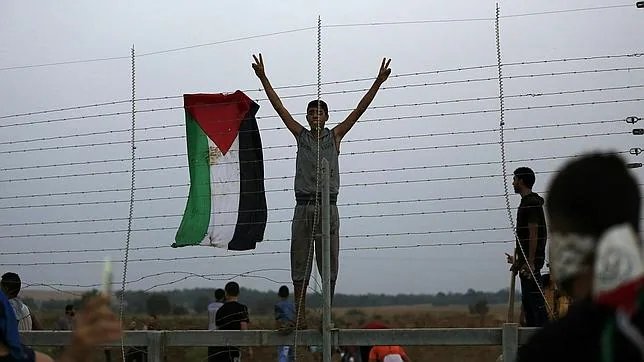 Un jóven palestino cuelga su bandera en la frontera