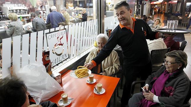 Un camarero de la cafetería Milán sirve una ración de churros a varias clientas