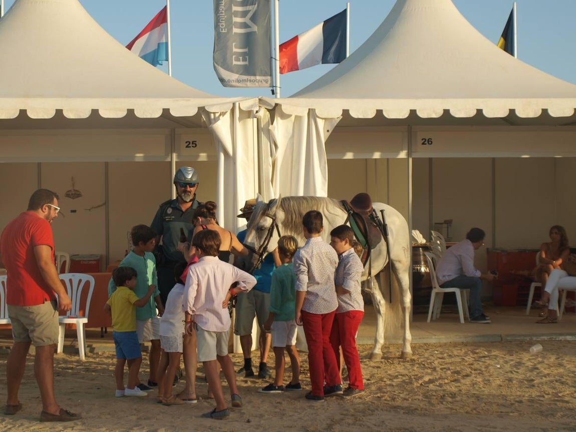 Estampa de unos niños acariciando un caballo de la Guardia Civil en las carpas
