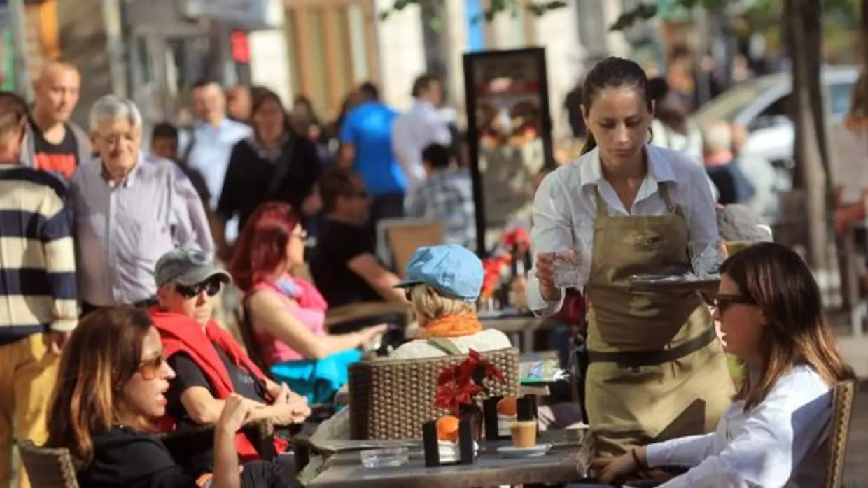 Una camarera sirve una mesa en la terraza de un bar