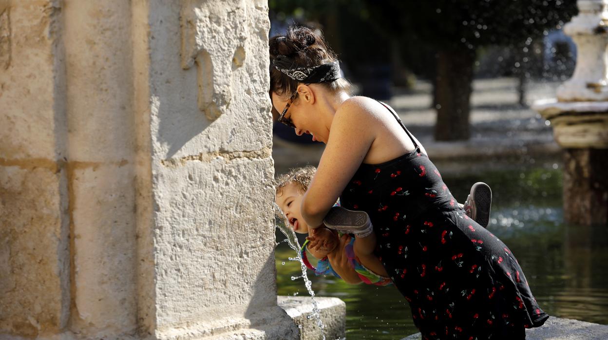 Una mujer da de beber a su hijo en una fuente de la ciudad