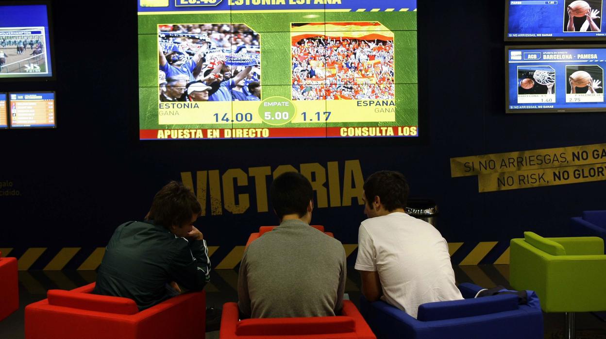 Tres jóvenes delante de una pantalla de fútbol en una casa de apuestas deportivas