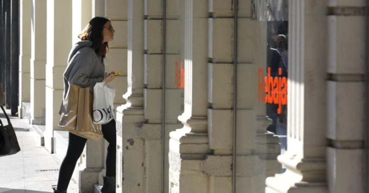 Una joven mira el escaparate de una tienda el primer día de rebajas de invierno