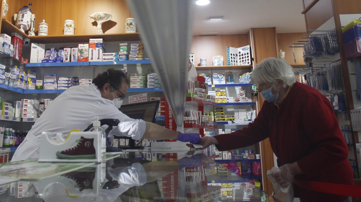 Un farmacéutico devuelve el cambio a una cliente en un establecimiento de Sevilla