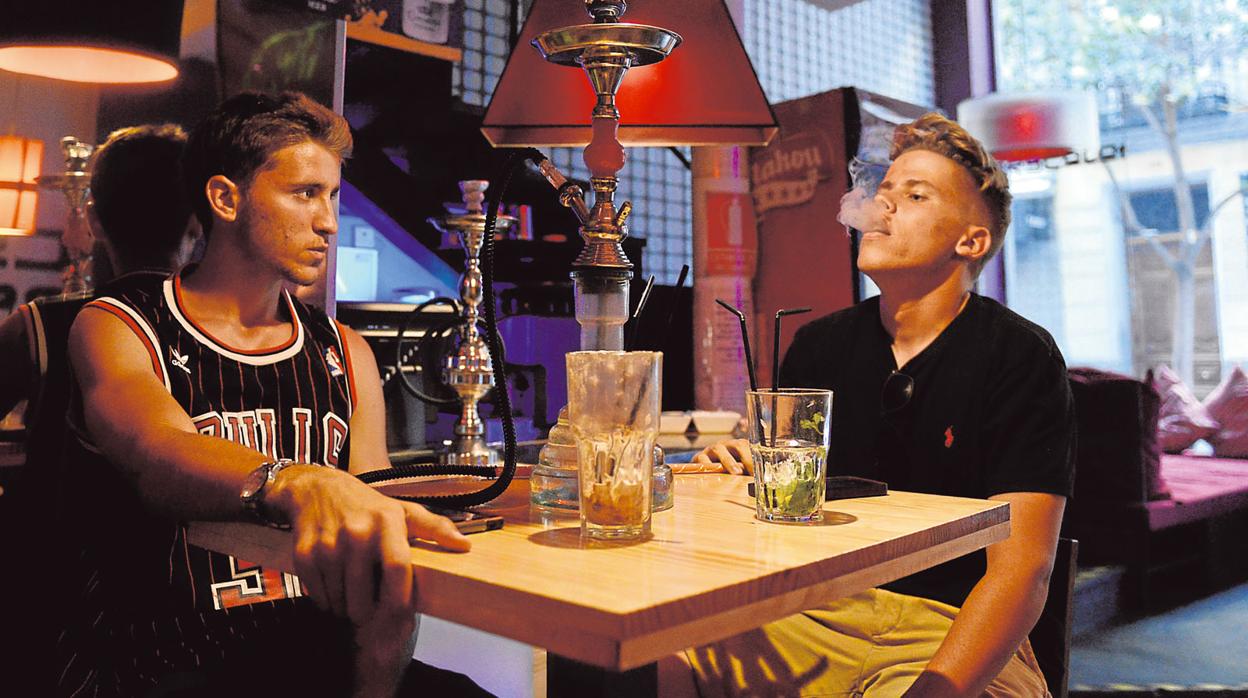 Dos jóvenes fumando en cachimba en un bar