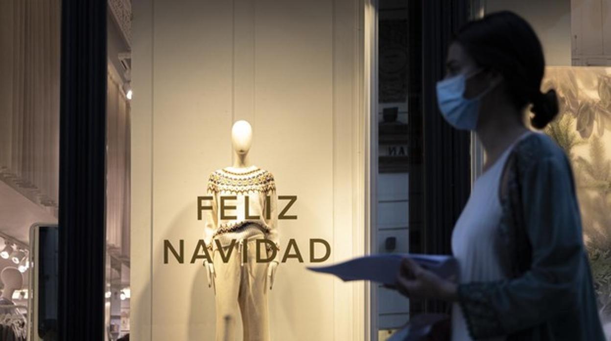 Una mujer pasa por un escaparate ya decorado con un mensaje para felicitar la Navidad en Sevilla