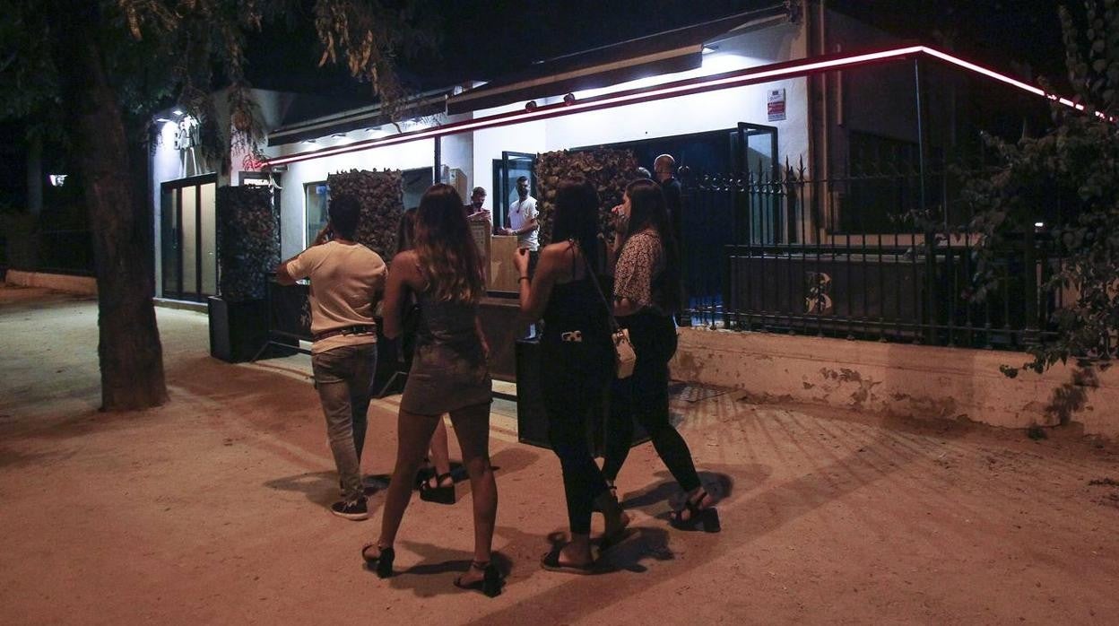 Varias personas pasean por la noche en Sevilla y pasan por la puerta de una discoteca