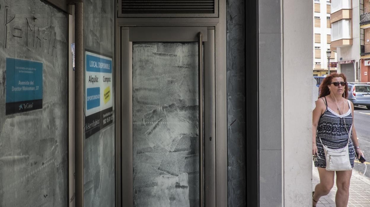 Una mujer pasa delante de una oficina de CaixaBank, disponible para alquiler o venta