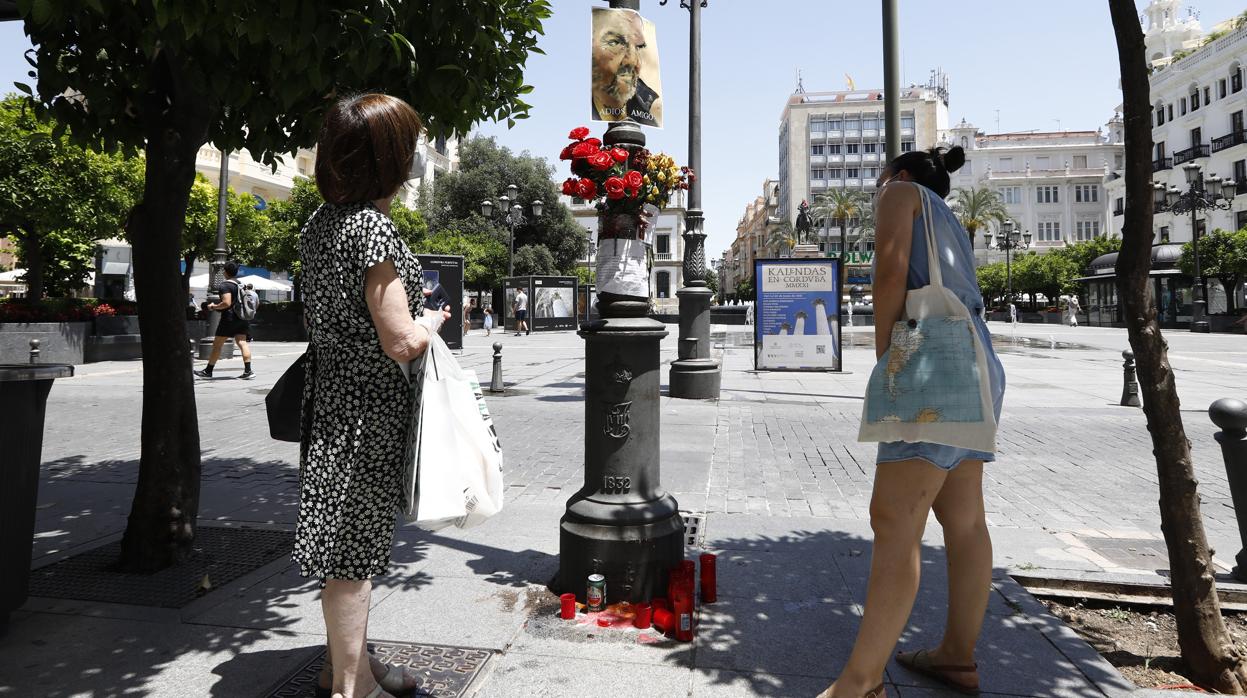 Dos mujeres miran la farola adornada en recuerdo de la persona sin hogar que pedía limosna en Las Tendillas