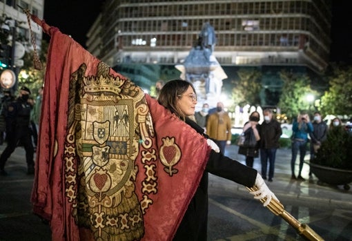 Lucía Garrido porta el estandarte real. Al fondo, la estatua de Colón junto a la Reina Isabel I en la plaza de los Reyes Católicos