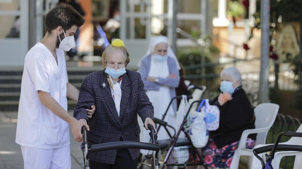 Imagen de archivo de un trabajador de una residencia de ancianos ayudando a caminar a una persona mayor