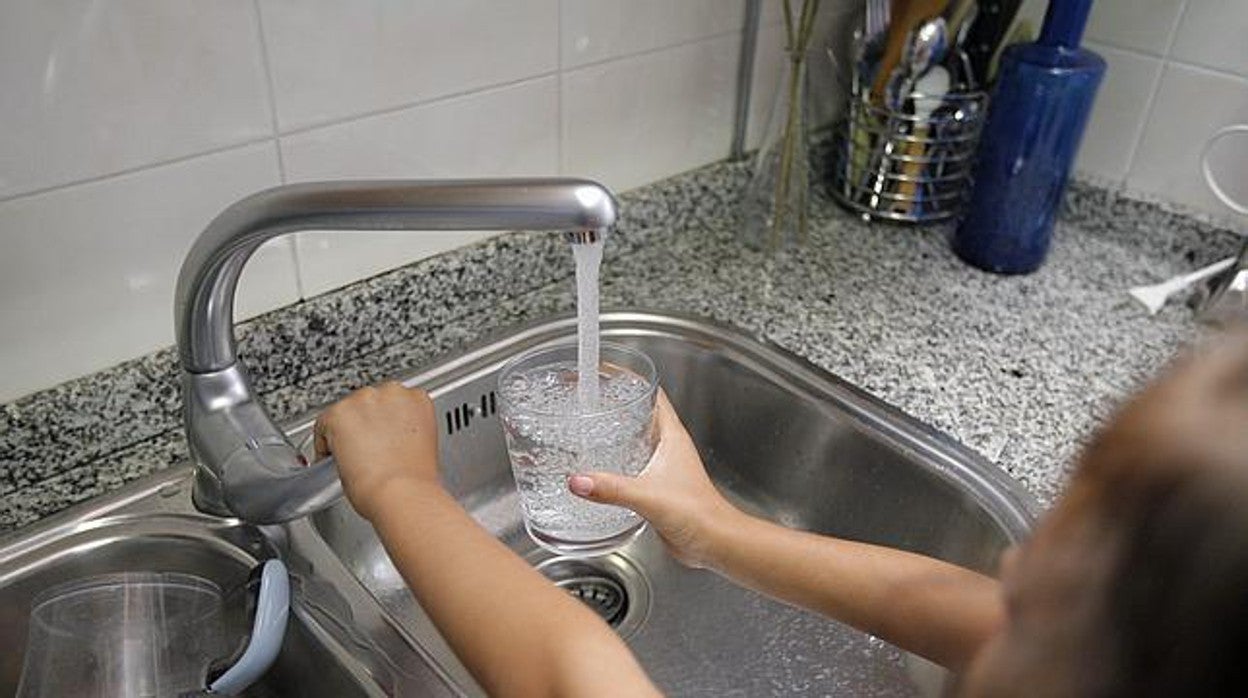 Una persona llena un vaso de agua con el grifo de una cocina