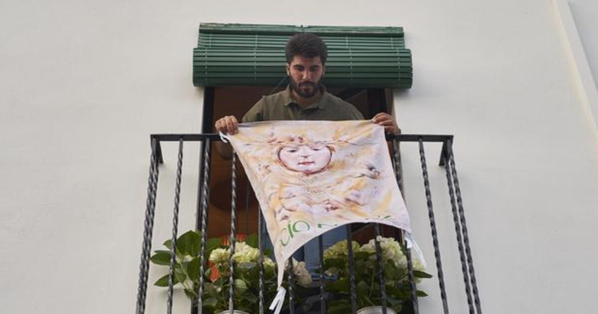Un joven almonteño coloca en su balcón una colgadura con la imagen d ela Virgen del Rocío