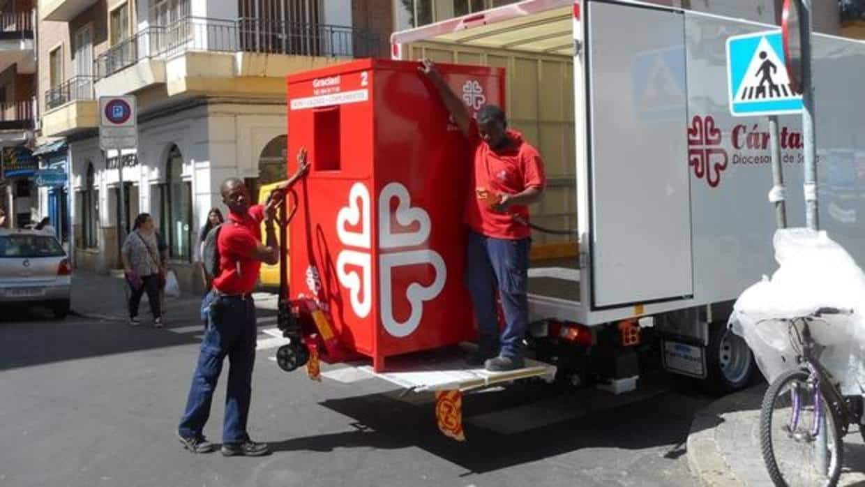 Dos empleados de Cáritas recogen un contenedor de ropa