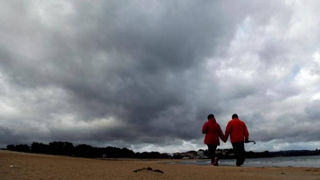 Una pareja pasea por la playa aprovisionados de un paraguas