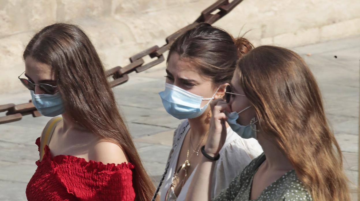 Tres jóvenes con mascarillas pasean por el entorno de la Catedral de Sevilla