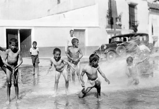 Un grupo de niños juega y se baña en plena calle con una manguera de riego en 1930
