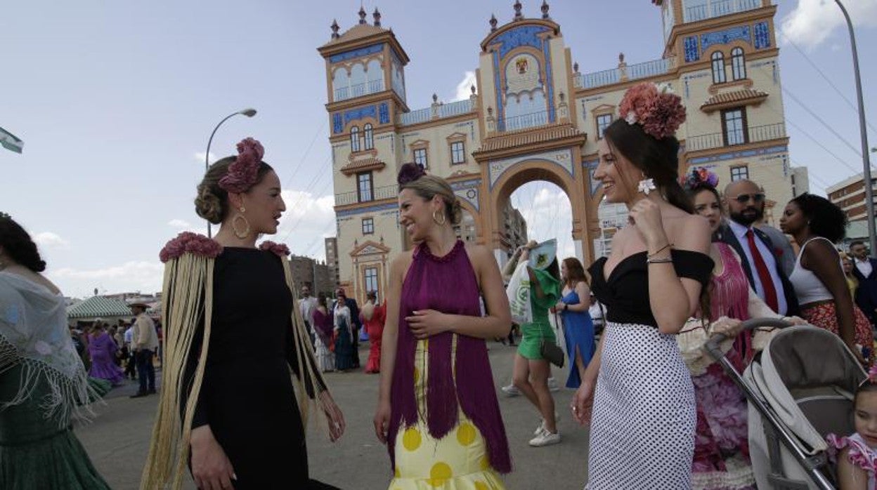 Tres mujeres vestidas de flamenca ante la portada de feria de 2022