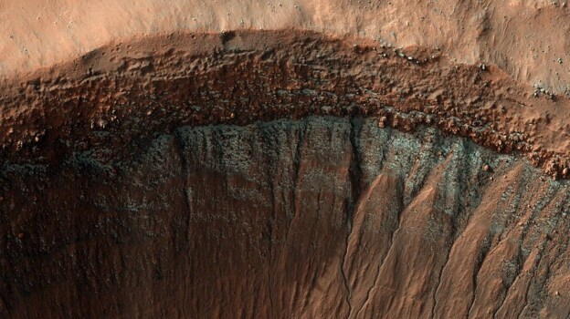 la cámara HiRISE capturó esta imagen del borde de un cráter en pleno invierno. La pendiente del cráter que mira al sur, que recibe menos luz solar, ha formado una escarcha brillante y en parches, que se ve en azul en esta imagen de color mejorado