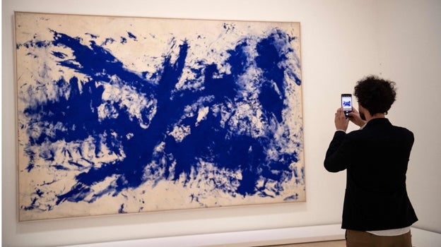 Un joven fotografía con su móvil una pintura de Yves Klein