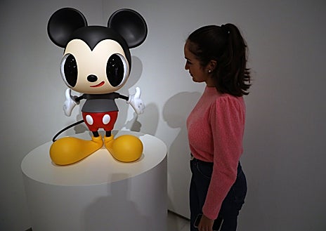 Imagen secundaria 1 - Sobre estas líneas, una joven contempla la versión de Calleja de Mickey Mouse. A la derecha, el artista traslada uno de sus cuadros. Arriba, Calleja entre dos de sus obras, una pintura y una escultura, en el Centro Cultural Fundación Unicaja