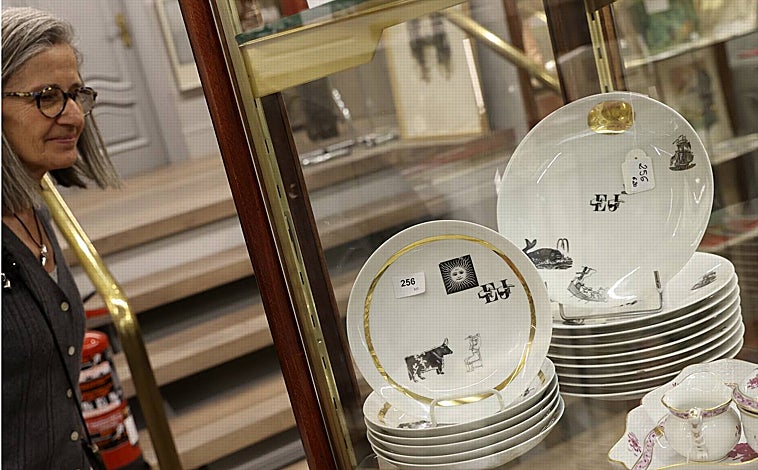 Imagen principal - Arriba, Consuelo Durán junto a parte de la vajilla de la boda de Jaime de Armiñán y Elena Santonja (lleva sus iniciales). Sobre estas líneas, a la izquierda, dibujo de Elena en la cocina y, a la derecha, Eduardo de Armiñán, junto a un mueble con piezas de cubertería que pertenece a la familia  