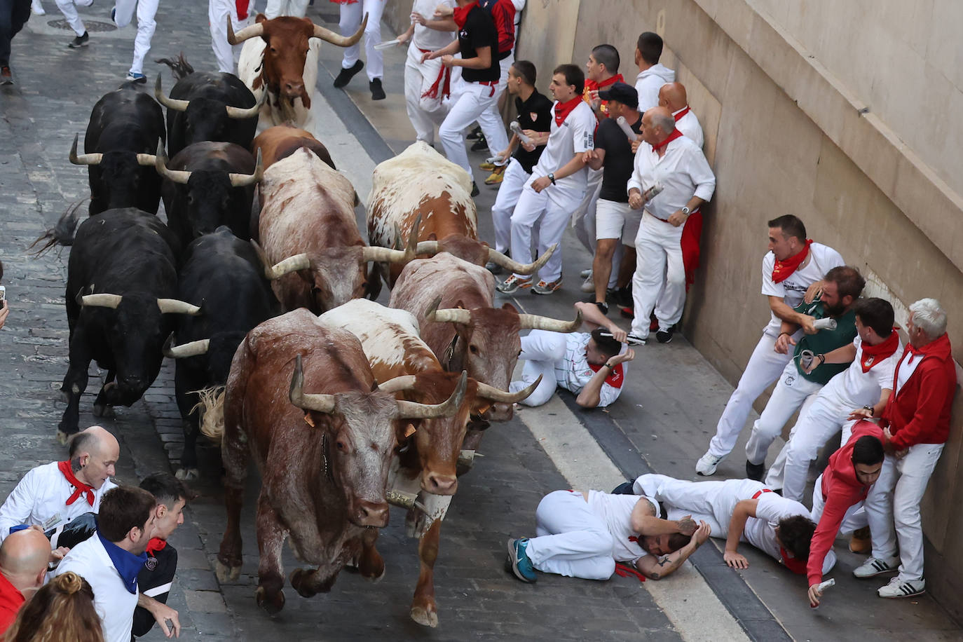 Varios mozos se cubren los rostros al caer al suelo durante el sexto encierro de las fiestas de San Fermín