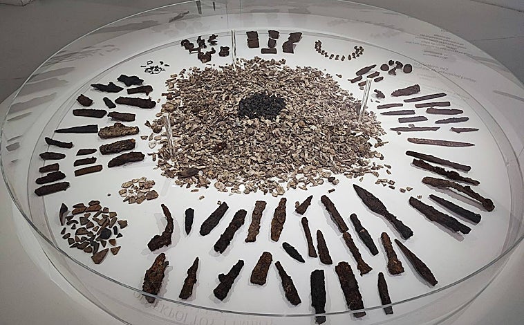 Imagen principal - Arriba lanzas y armas herrumbrosas, botones de hueso y rascadores hallados entre los cuerpos. Debajo, restos de un escudo destrozado por el paso de 24 siglos y algunos restos humanos tal como se hallaron en el poliandrion