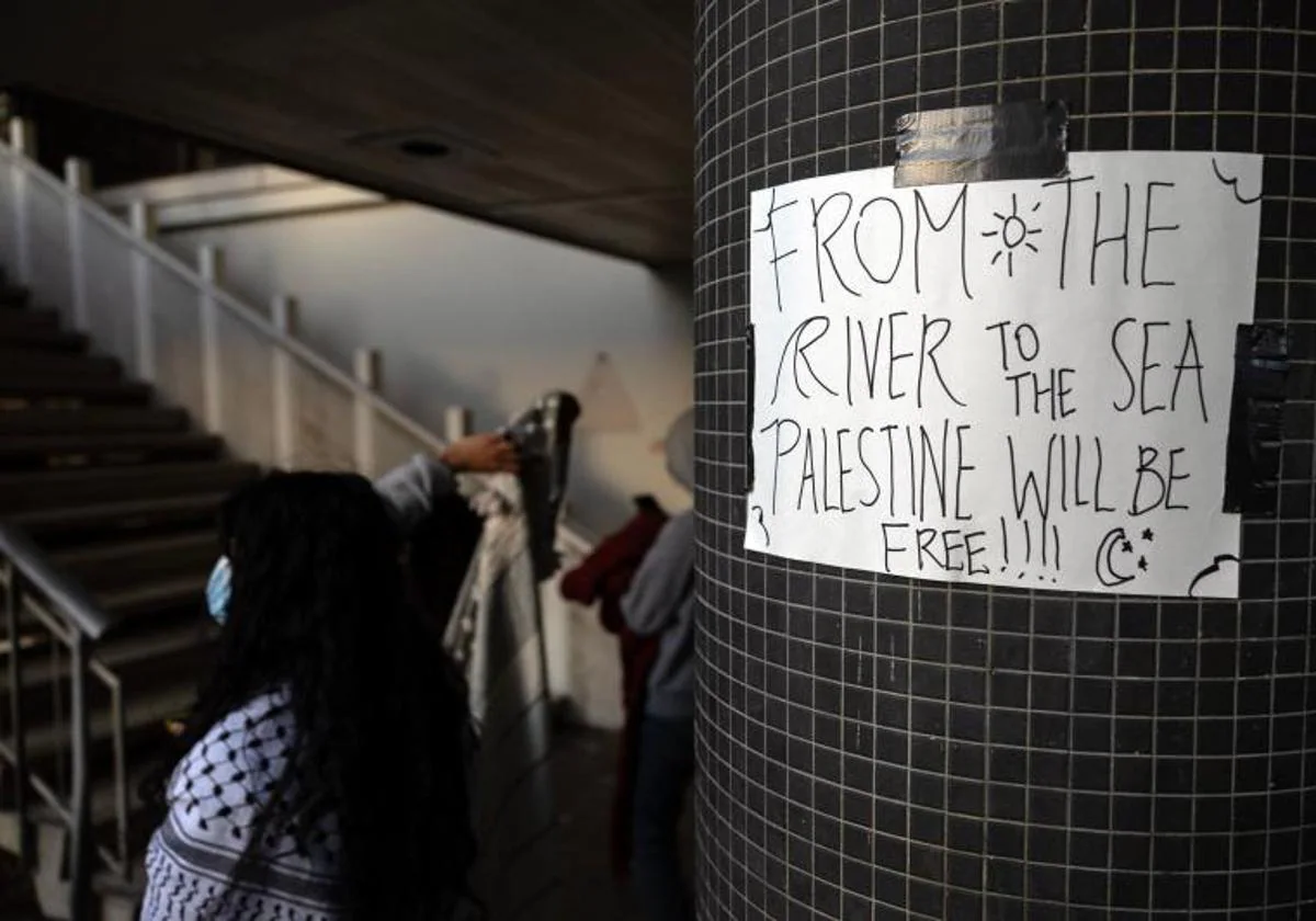 Manifestantes propalestinos esperan bajo un cartel en el que se lee 'Del río al mar Palestina será libre' pegado en una columna de la comisaría de Van Nuys del Departamento de Policía de Los Ángeles