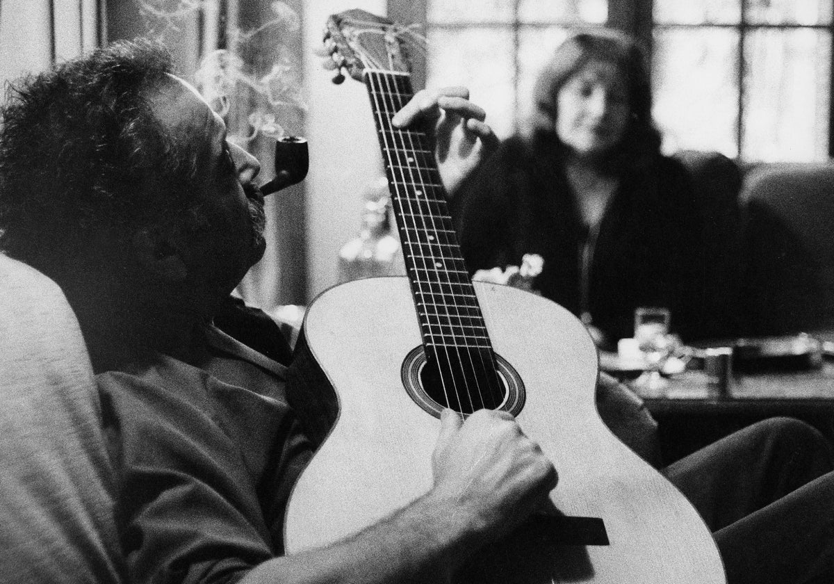 Brassens tocando la guitarra mientras fuma en pipa