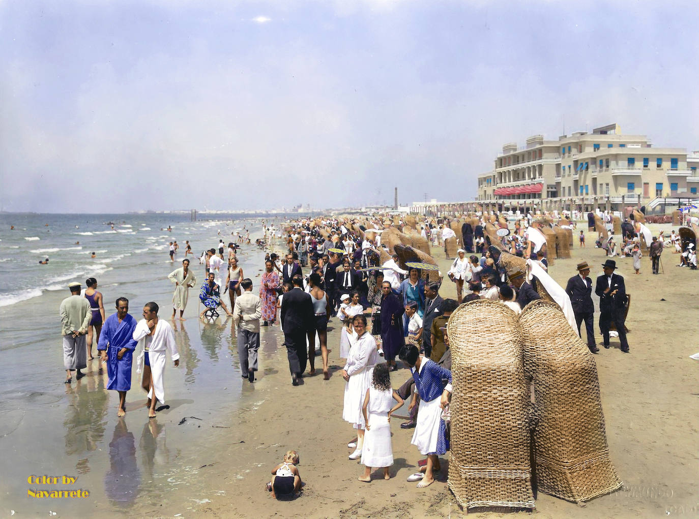 Playa de la Victoria (Cádiz, 1929). Mucha gente en la playa, demasiados trajes y demasiada ropa. Muchos niños con sus niñeras. Durante mucho tiempo, para muchos varones fue un problema mostrar el torso. De modo que usaban camisetas de tirantes. Y por lo que vemos en la imagen, gustaba mucho en Cádiz el uso del albornoz en la playa.