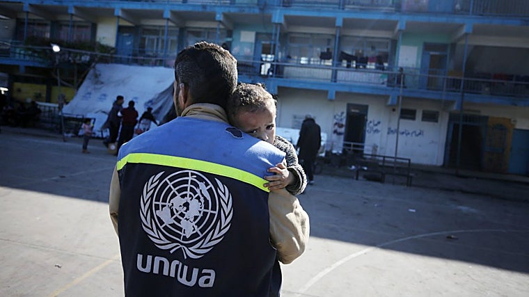 Un trabajador humanitario de UNRWA carga a un niño herido en el patio de una escuela convertida en refugio en el centro de Gaza, enero de 2024