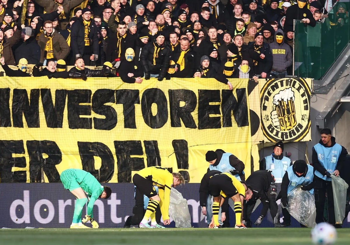 Los jugadores del Borussia Dortmund ayudan a retirar objetos caídos al campo